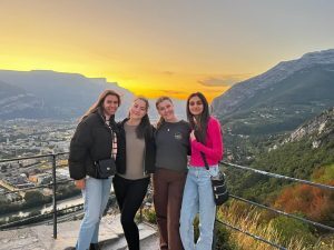 Four people standing together at a mountain viewpoint during sunset, overlooking the city and surrounding valleys.