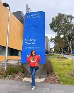 Marketing and Management student Ella standing in front of the Monash University Caulfield Campus sign in Melbourne, Australia