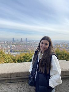 Lauren standing at a viewpoint above Grenoble, with the city and distant towers visible below.