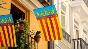 A Valencia flag strung between buildings, with potted plants and balconies in the background.